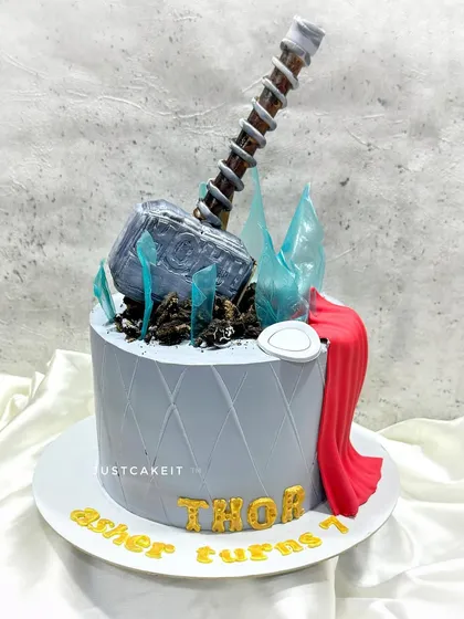 A Thor-themed cake with a completely edible Mjolnir hammer. The broken ice effect is made from sugar glass, adding a dynamic touch to this superhero cake.