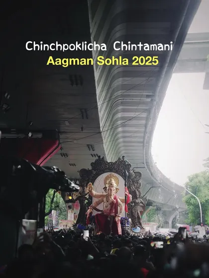 A ground-level view of the Chinchpoklicha Chintamani Aagman, framed by an overpass. This shot creates a dramatic sense of scale, showing the idol emerging into the city.
