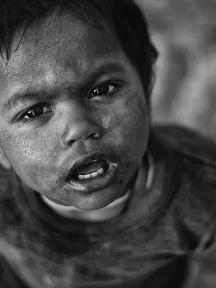 This powerful black and white portrait of a young child looking directly up at the camera is filled with raw emotion. The high-contrast monochrome effect highlights the dirt on his face and the intensity in his eyes, creating a truly unforgettable image.