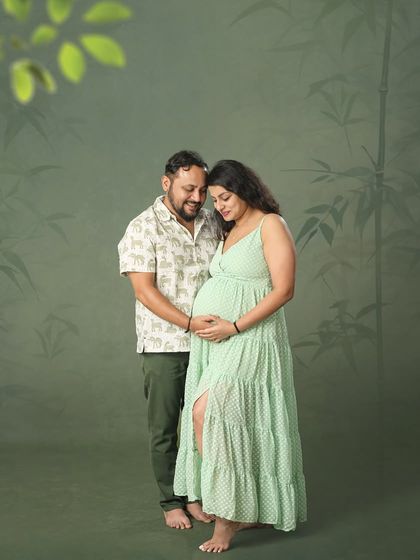 A quiet, loving moment between expectant parents. The soft green tones of their outfits and the backdrop create a serene and peaceful atmosphere for this maternity photo.