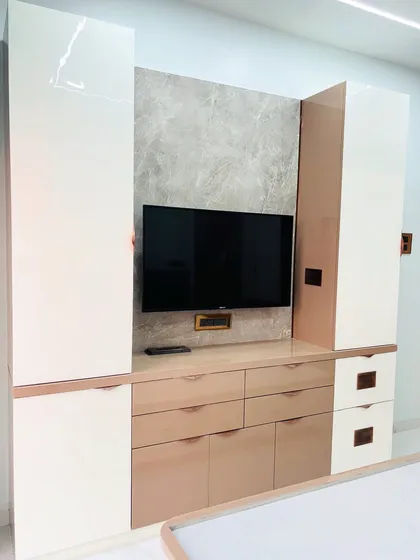 The TV and storage unit in the bedroom, designed with a mix of high-gloss white and beige laminates. The unit provides ample drawer space and a clean backdrop for the television.