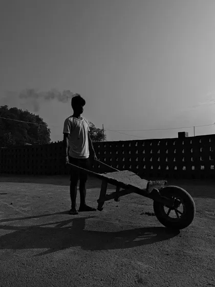 A young worker stands with a wheelbarrow in the stark light, his silhouette creating a powerful and contemplative black and white portrait.