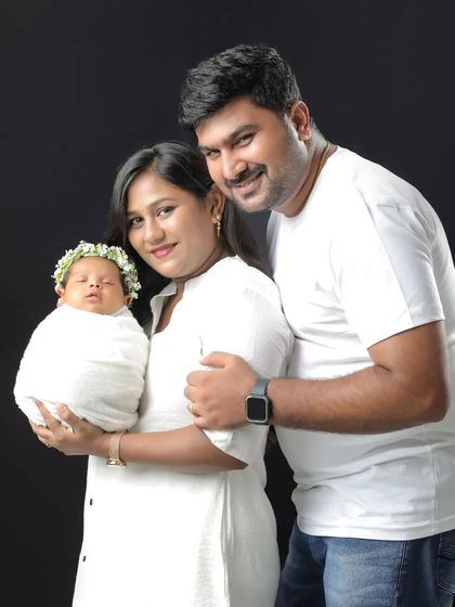A gorgeous family of three. The parents are beaming with pride as they hold their precious newborn, all dressed in white for a classic family portrait.