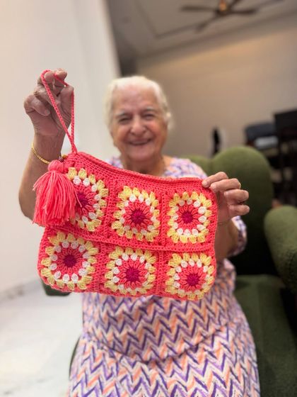 Dadi holding our vibrant pink and yellow granny square pouch. It's perfect for makeup, stationery, or any other essentials.