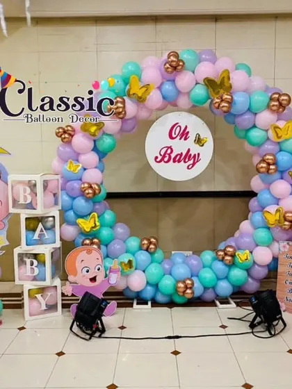 A full view of a baby shower photo booth, featuring a circular balloon arch, 'BABY' blocks, and large, cute character cutouts.