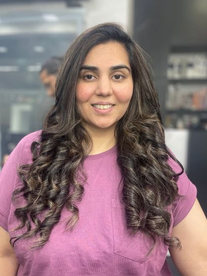 This client is happy with her new look, featuring long hair styled in tight, bouncy curls with subtle highlights.