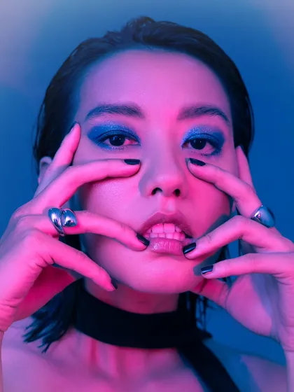 An intense close-up where the dual-toned lighting highlights the bold blue eyeshadow and the model's features. The framing is tight to create a sense of intimacy and impact.