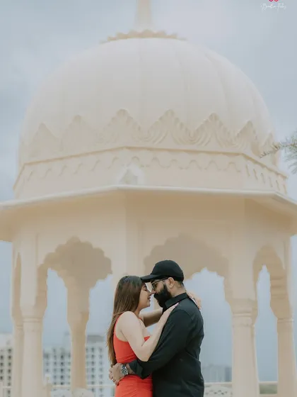 A romantic pre-wedding portrait of a couple framed by the beautiful architecture of a white marble gazebo, creating a classic and elegant feel.