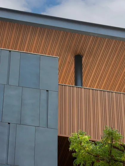 A detail of the grey aluminum cassette panels and wood-look fluting on the Poorvi Marg project. The combination of materials creates a sophisticated and modern aesthetic.