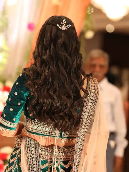 A look at the beautiful, cascading curls and hair accessory for this reception look. The hairstyle was designed to complement her elegant, heavy lehenga.