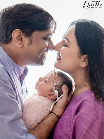 A sweet family portrait with parents touching noses while holding their newborn baby.