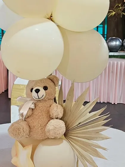 A charming teddy bear centerpiece for a baby shower. A cute teddy bear holds a bouquet of neutral-colored balloons, perfect for decorating guest tables.