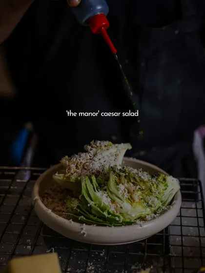 A final drizzle of dressing over my Manor Caesar Salad. This dish is a favorite for a reason, and if you haven't tried it, you're seriously missing out.