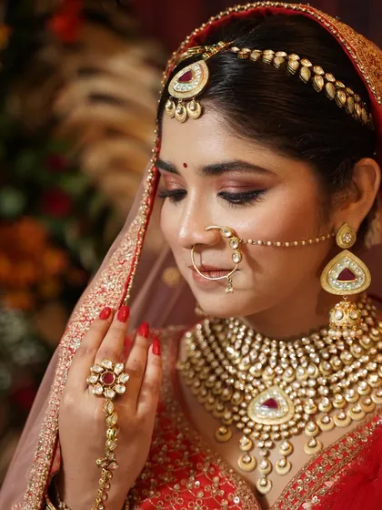 A close-up detail shot focusing on the eye makeup and traditional jewelry. The soft, sparkly eyeshadow adds a touch of glamour to the classic red bridal look.