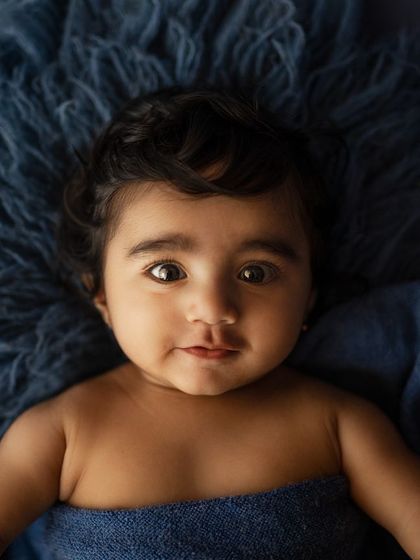 This little cutie pie is lying on a blue fur rug, looking right at the camera with so much expression.