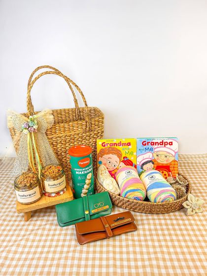 A gift hamper curated for grandparents, featuring books, snacks, and other thoughtful items. The checkered background and wicker basket give it a warm, homely feel.