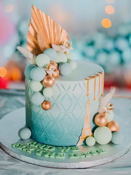 A stunning blue engagement cake with a geometric pattern, gold drip, and an Eiffel Tower detail. The sphere clusters and pampas grass add a modern, celebratory touch.