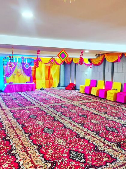 This shows the spacious floor seating arrangement for a religious event. The area is carpeted, and the stage is set up at the far end, ready for the kirtan or puja.
