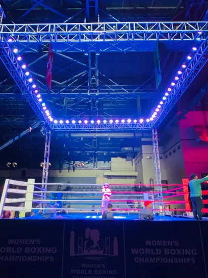 A view of the boxing ring with its overhead lighting rig, ready for action. The setup ensures perfect visibility for judges, spectators, and television cameras.
