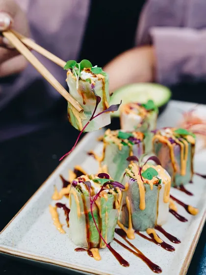 A vibrant shot of summer rolls being picked up with chopsticks. The focus is on the fresh ingredients and the colorful sauces, making it look like a light and delicious appetizer.