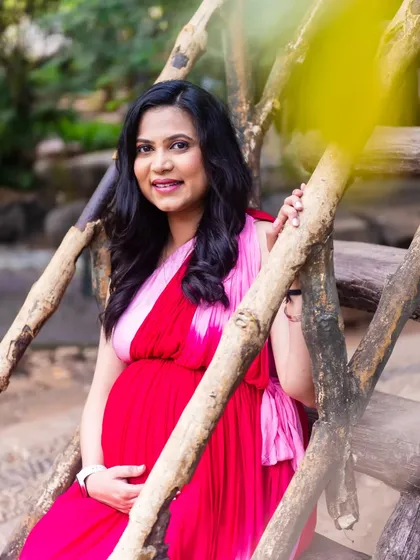 A beautiful, framed shot of the mom-to-be on a wooden bridge, looking serene and happy in her red and pink gown.
