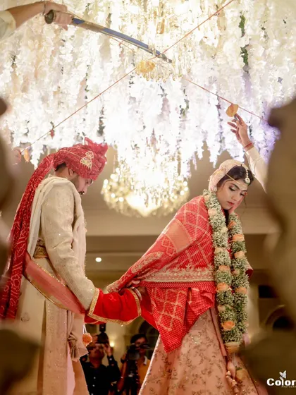 A significant moment during the wedding ceremony, with the couple's garments tied together as they perform the rituals under a stunning floral chandelier.