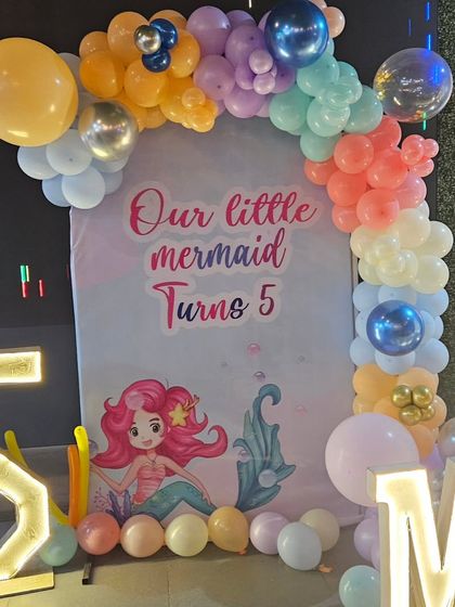 The main backdrop for the mermaid party, featuring a beautiful balloon arch and a personalized "Our little mermaid Turns 5" banner.