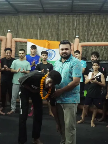 A coach honors a victorious fighter with a garland in front of the team and the Indian flag.