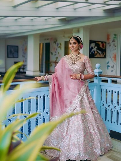 A portrait of the bride on a balcony, showcasing her complete look. The soft pink tones in her makeup and outfit create a harmonious and romantic bridal style.