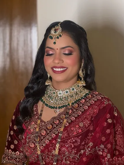 A bride fit for royalty. This reception look in a deep maroon velvet lehenga features a bold lip and shimmery eyes, perfect for an evening of celebration.