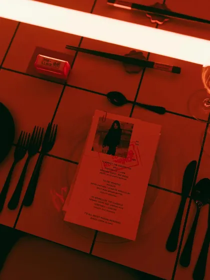The table setting for Rohan's 30th, featuring a personalized menu with his photo, set against a modern, tiled tabletop under red neon light. The vibe was cool, personal, and a little bit extra.