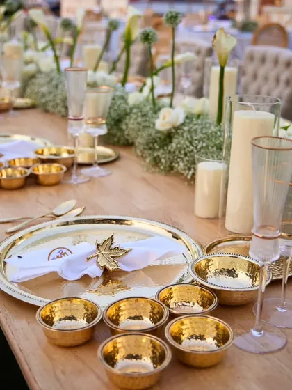 A close-up of a luxurious sit-down dinner setting. The golden bowls and plates, paired with elegant glassware, create an opulent and regal dining experience.