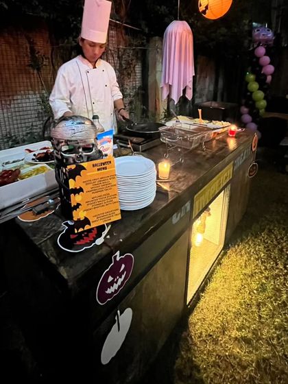 A chef preparing food at the Halloween live station. The setup includes spooky decor like a skull and a printed menu, ensuring the theme is consistent throughout the event.