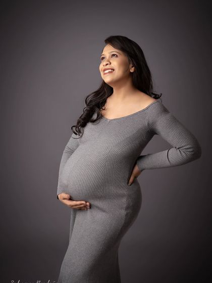 A portrait of hope and anticipation. The mom-to-be looks up with a joyful expression, her hands cradling her bump, dressed in a simple and stylish grey ribbed gown.