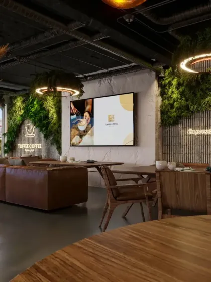 A wide shot of the cafe interior, showing the mix of comfortable lounge seating and dining tables. The large screen and neon sign add modern, dynamic elements to the rustic design.