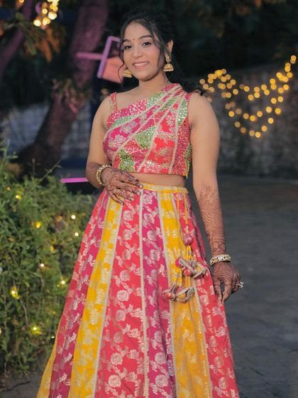 A client looking joyful in a bright pink and yellow lehenga, perfect for a fun Haldi ceremony.
