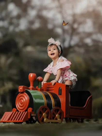 A moment of pure, uninhibited joy. This little girl's laughter is infectious as she plays on the toy train, with a butterfly fluttering by.