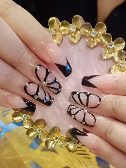 A creative butterfly wing design using black polish and rhinestones over a neutral base. This is a unique and artistic take on embellished nails.