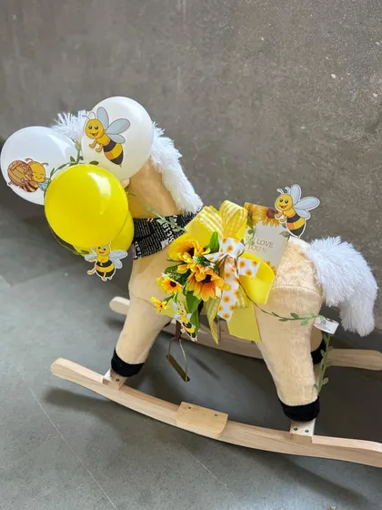 A whimsical and grand gesture for a baby announcement. We've transformed a classic rocking horse into a stunning gift platform, adorned with a bee-themed balloon bouquet and other sweet surprises.