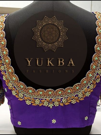 The back of a rich purple blouse with a scalloped U-neckline. The entire border is heavily worked with gold zardosi and light blue thread, creating a beautiful contrast.