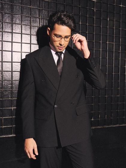 A more relaxed pose in the same powerful suit. Here, Siddhant Chaturvedi adjusts his glasses, adding a touch of personality to the formal styling.