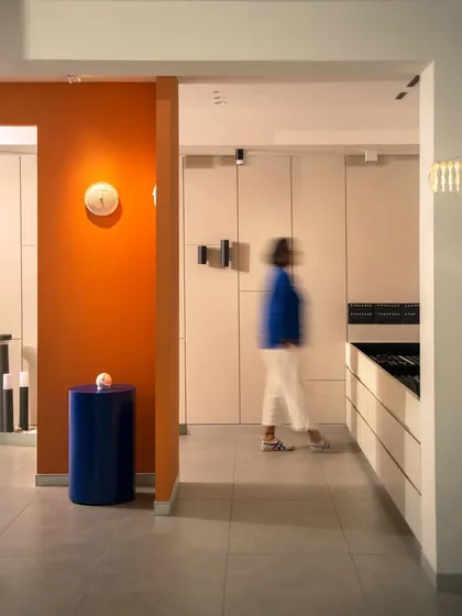 The layout is designed for easy navigation, with clear sightlines through different zones. This view captures the interplay of color, from the orange wall to the blue pedestal, against a clean, white canvas.