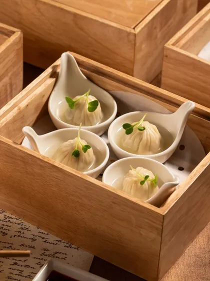 A clean, minimalist shot of soup dumplings in a wooden box. The simple composition draws all attention to the food itself.