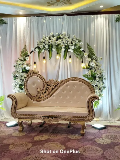 A beautiful stage setup for a baby shower with a white and green theme. The circular floral arch is decorated with white gerberas and green leaves, complemented by hanging Edison bulbs.