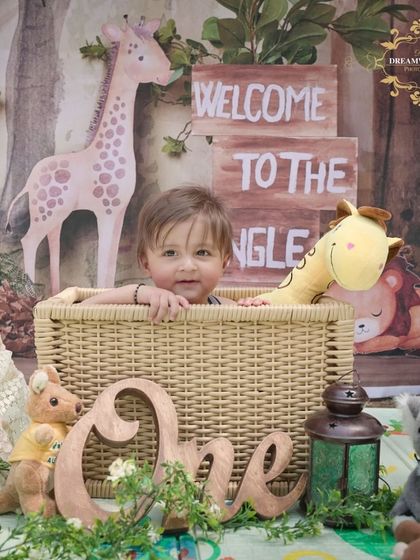 A "Welcome to the Jungle" first birthday theme. This little one is sitting in a basket surrounded by stuffed animals, creating an adorable and adventurous scene.