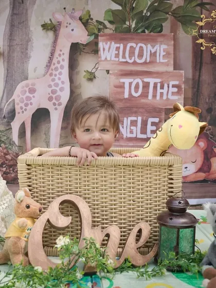 A "Welcome to the Jungle" first birthday theme. This little one is sitting in a basket surrounded by stuffed animals, creating an adorable and adventurous scene.