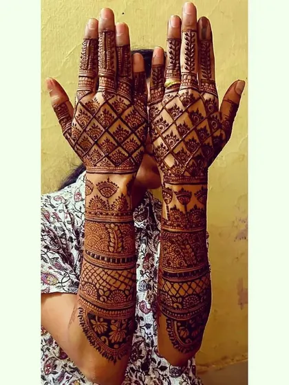 A full-coverage design with a prominent diamond-shaped jaal pattern on the back of the hands. The forearms are decorated with bands of traditional Indian art, creating a very rich and dense look.