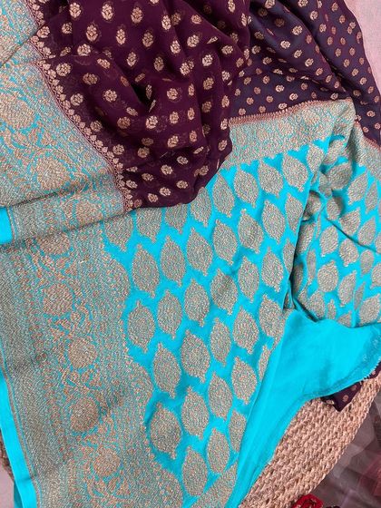 The pallu of the wine-purple and sky blue Kadi georgette saree, showcasing the intricate leaf-patterned weaving that gives it a luxurious feel.