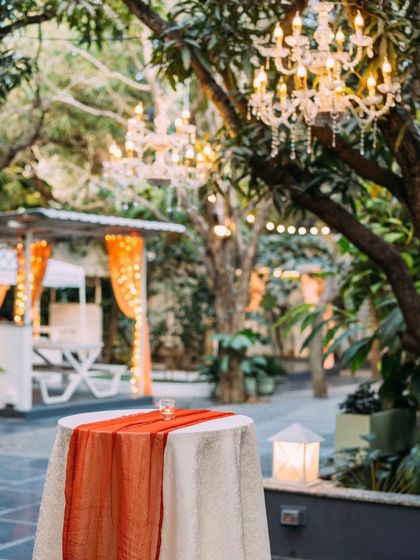 A detail shot of the cocktail party decor. A crystal chandelier hangs from a mango tree over a high table, blending rustic charm with timeless elegance.