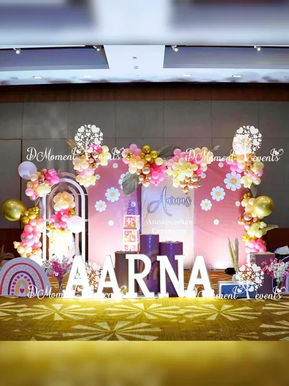 The main stage for Aarna's Boho Rainbow Annaprashan. The setup features marquee letters, a daisy-adorned backdrop, and beautiful balloon arrangements in a soft, warm color palette.